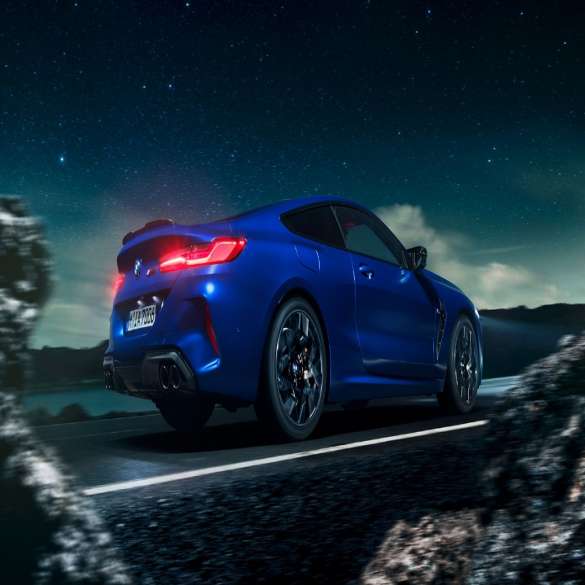 BMW M8 Coupé, three-quarter side view. BMW M8 Coupé in Marina Bay Blue metallic, driving three-quarter side view in front of starry sky.