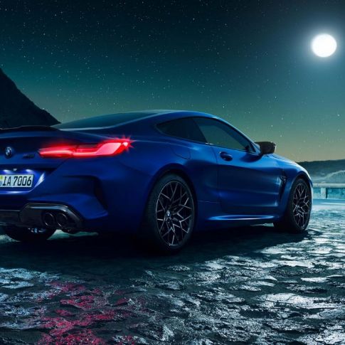 BMW M8 Coupé, three-quarter rear view. BMW M8 Coupé in Marina Bay Blue metallic with illuminated LED rear lights, standing three-quarter rear view with full moon.