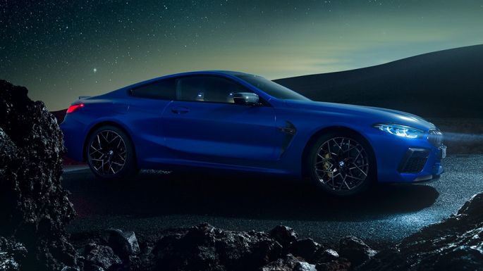 BMW M8 Coupé, three-quarter side view. BMW M8 Coupé in Marina Bay Blue metallic, standing three-quarter side view at night.