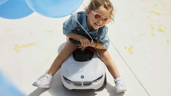 A girl with pink sunglasses and a blue balloon sits happily on a BMW Baby Racer. A girl with pink sunglasses and a blue balloon sits happily on a BMW Baby Racer.