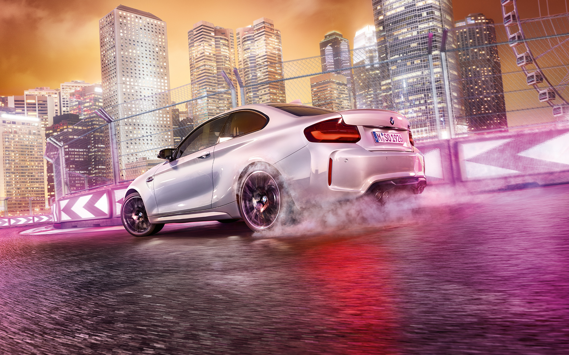 BMW M2 Competition accelerates White BMW M2 Competition drifting on race track in front of nocturnal skyline.