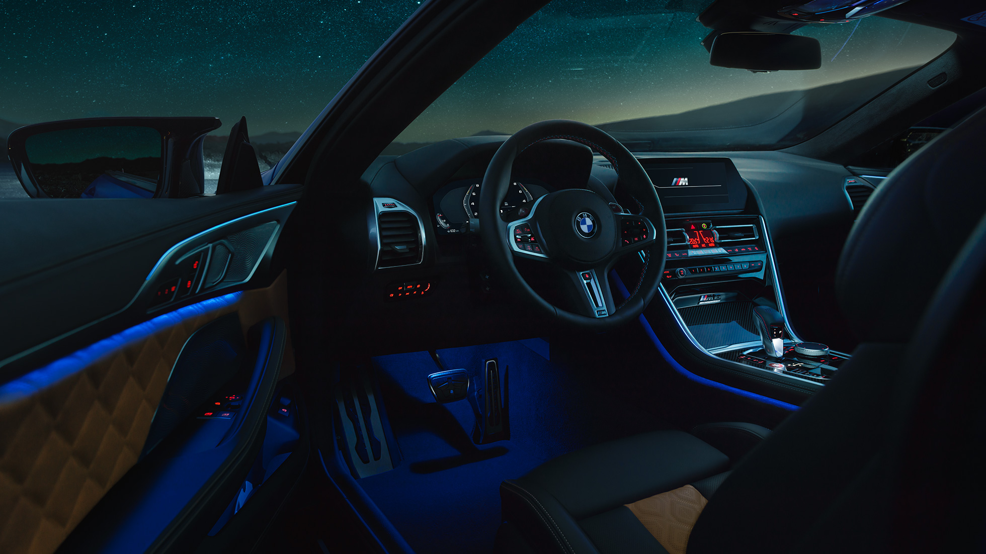 Interior BMW M8 Coupé. BMW M8 Coupé, interior at night with M leather steering wheel and blue ambient light with open driver door.