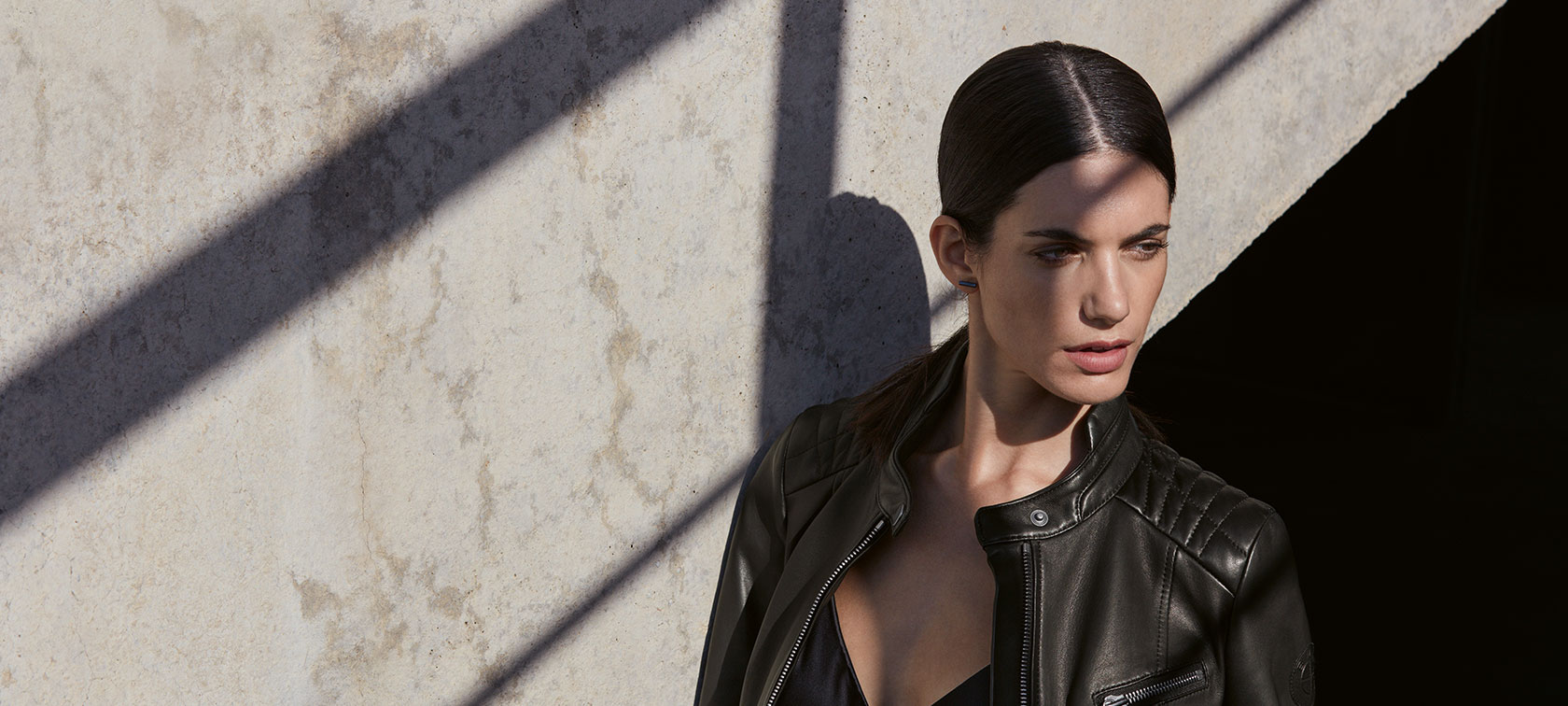 Defining Life and Style. In the picture, a young woman is wearing theBMW Ladies Leather Jacket in front of an urban backdrop.