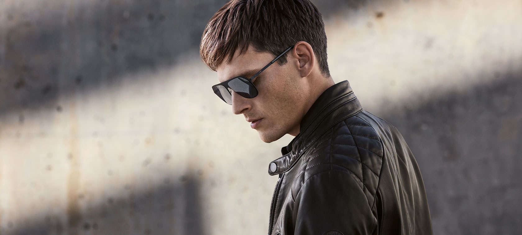 A model looking down is wearing BMW Sunglasses and a BMW Men's Leather Jacket. A model looking down is wearing BMW Sunglasses and a BMW Men's Leather Jacket.