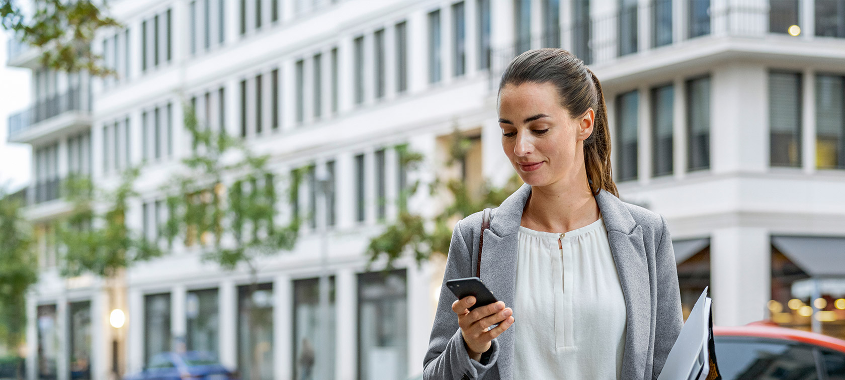 Remote Software Upgrade Woman standing in front of building looking at her smartphone