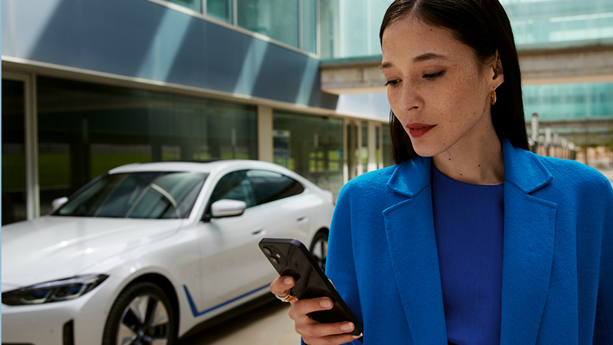 Woman standing in front of a BMW Woman standing in front of a BMW and looks at her smartphone