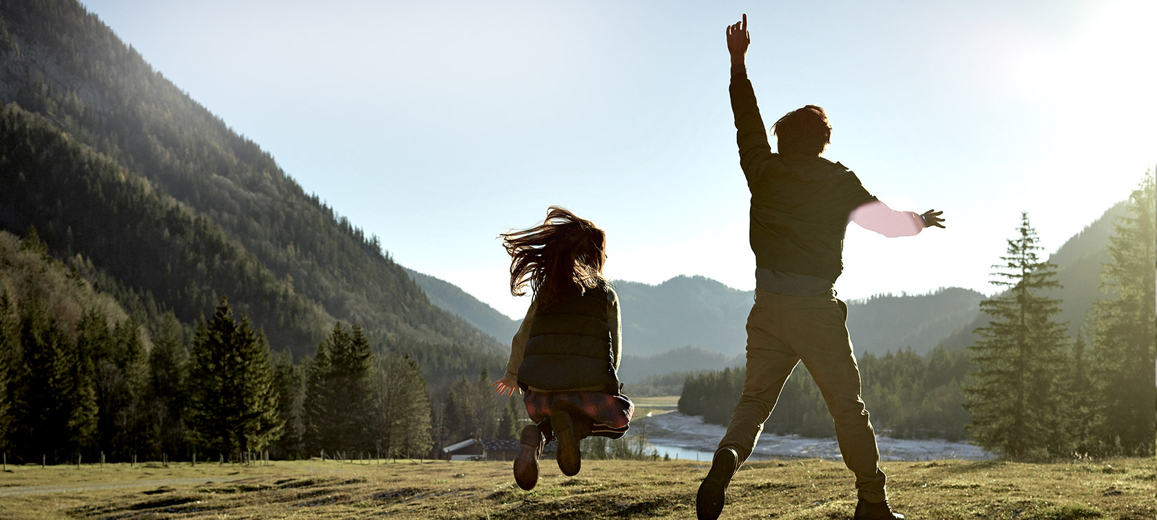 Man and girl jumping on meadow in mountain valley, rear view Man and girl jumping on meadow in mountain valley, rear view