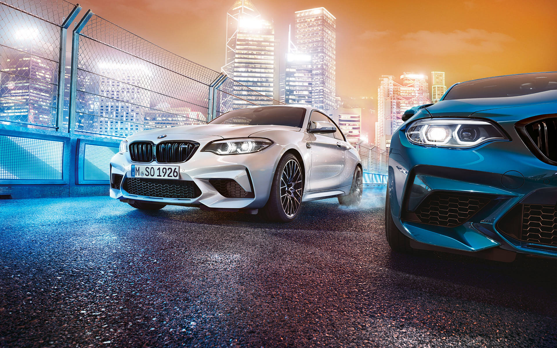 White and blue BMW M2 Competition while stationary White and blue BMW M2 Competition in front view standing in front of nocturnal cityscape.