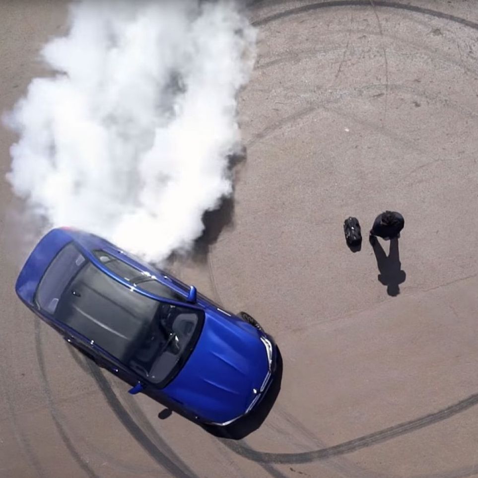 A car burns rubber around a male model with a bag from the BMW M Collection. A car burns rubber around a male model with a bag from the BMW M Collection.